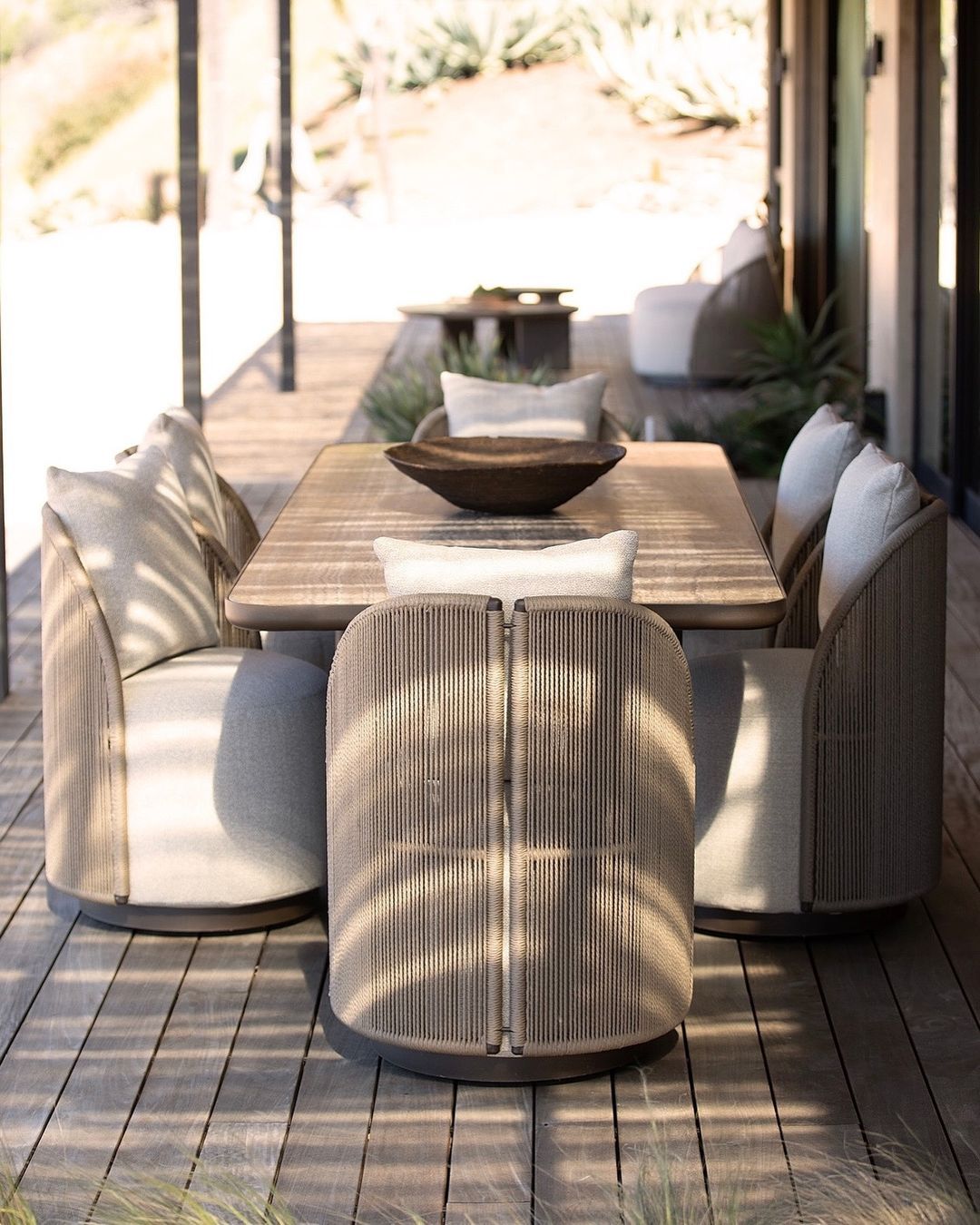 Corda hand woven outdoor dining chairs surrounding dark rectangular table on sunlit terrace — natural rope texture and cream linen upholstery — minosé