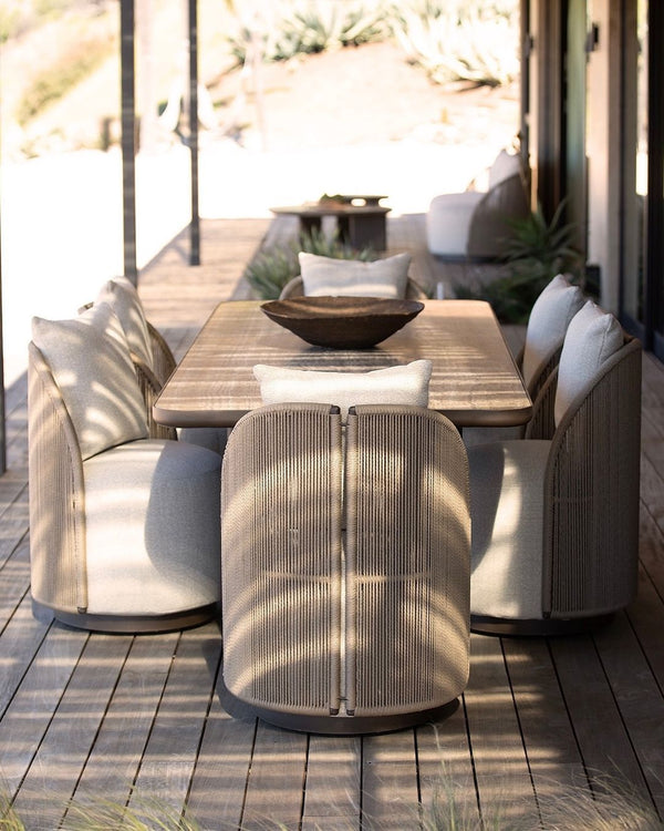 Corda hand-woven outdoor dining chairs surrounding dark rectangular table on sunlit terrace — natural rope texture and cream linen upholstery — Minosé