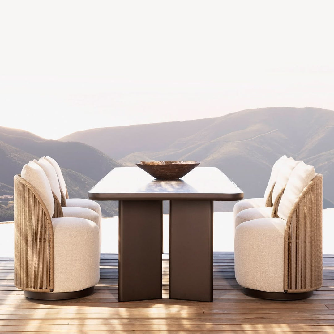 Corda woven outdoor dining chairs paired across sculptural dark table with mountain backdrop — luxury terrace seating — Minosé